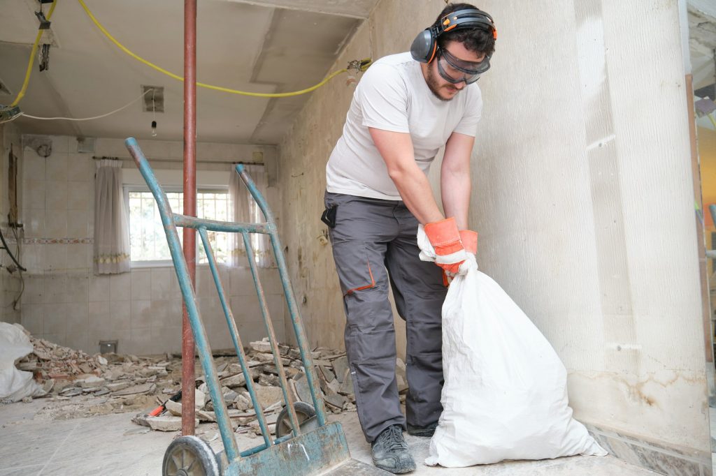 Builder collecting construction debris in a bag, and carrying in a hand trolley. House renovation.